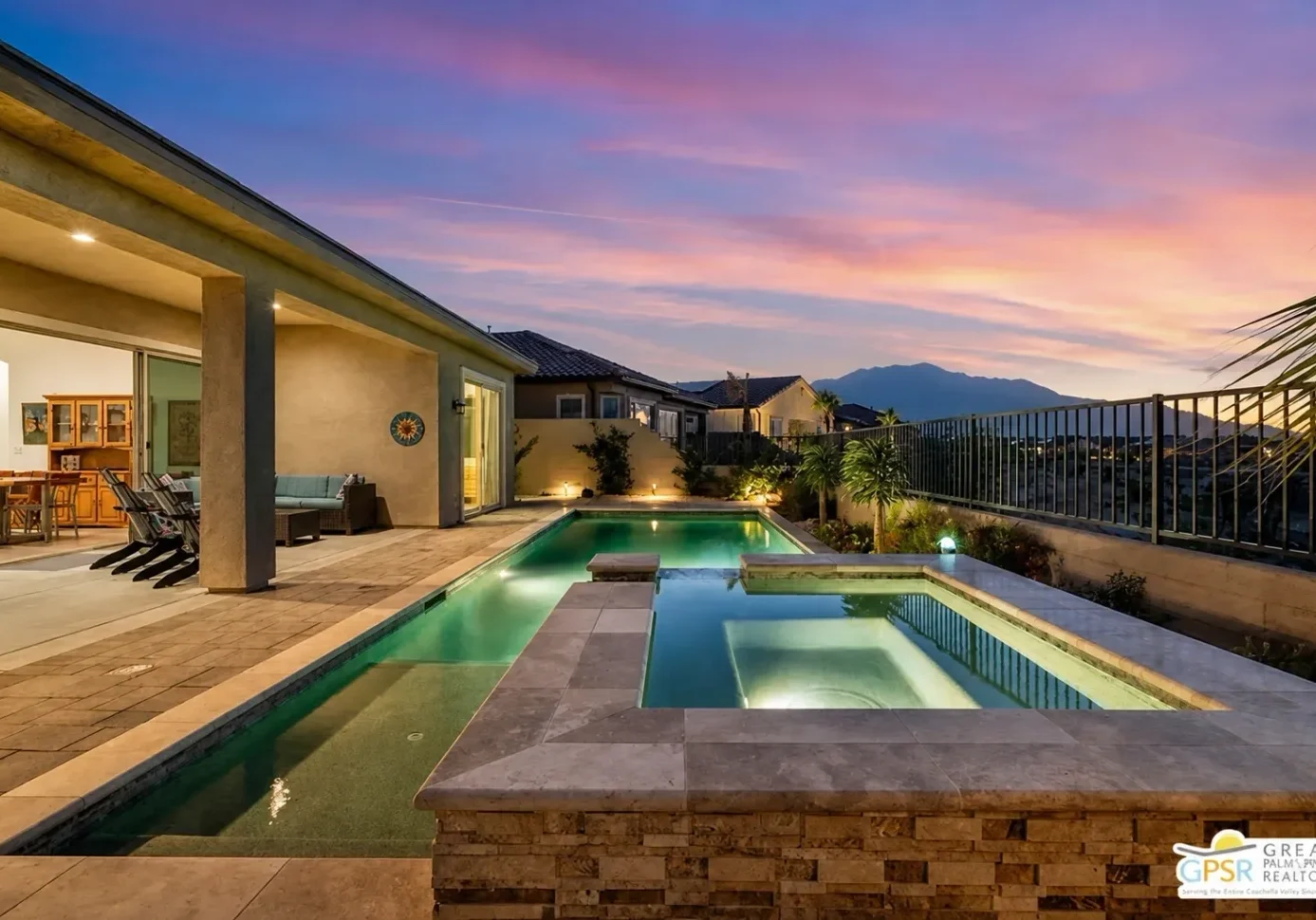 Swimming pool in the backyard of a home at dusk, surrounded by a fence, plants, trees